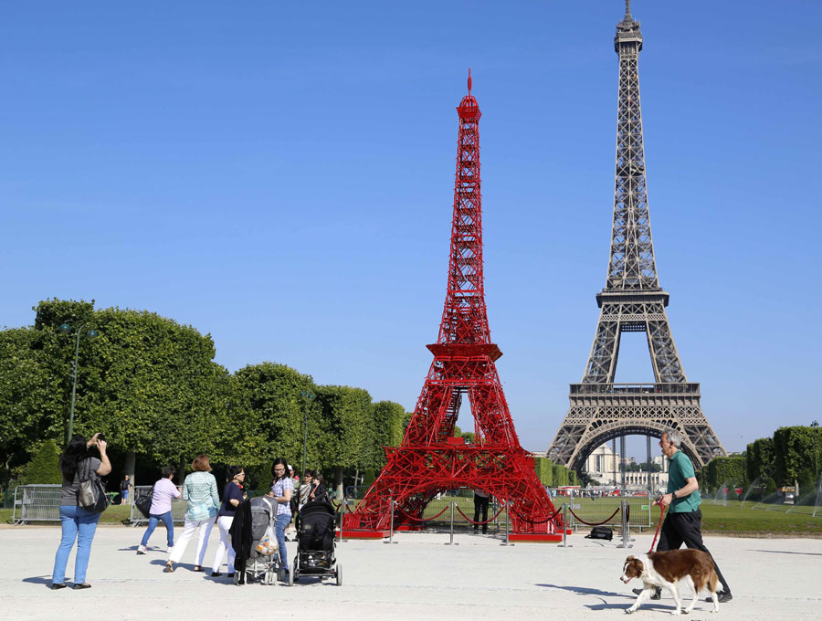 Des passants s'arrêtent pour observer une réplique de la Tour Eiffel construite avec des chaises de bistrot rouges, pour marquer le 125e anniversaire des chaises de bistrot de l'entreprise Fermob, à Paris, le 24 juin 2014. Tout comme la Vieille Dame, les fameuses chaises de bistrot célèbrent cette année leur 125e anniversaire. [Photo / agences] 
