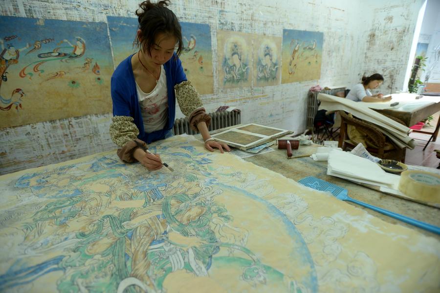 Une jeune peintre dessine une peinture murale dans un studio de la commune de Yuequan, à Dunhuang, dans la Province du Gansu (Nord-ouest de la Chine), le 27 juin 2014. Attirés par l'art des peintures murales des Grottes de Mogao, de plus en plus de jeunes artistes viennent à Dunhuang pour apprendre la création de peintures murales et ouvrir leurs propres studios. [Photo / Xinhua]