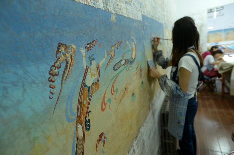  Une jeune peintre au travail sur une peinture murale dans un studio de la commune de Yuequan, à Dunhuang, dans la Province du Gansu (Nord-ouest de la Chine), le 27 juin 2014. Attirés par l'art des peintures murales des Grottes de Mogao, de plus en plus de jeunes artistes viennent à Dunhuang pour apprendre la création de peintures murales et ouvrir leurs propres studios. [Photo / Xinhua]
