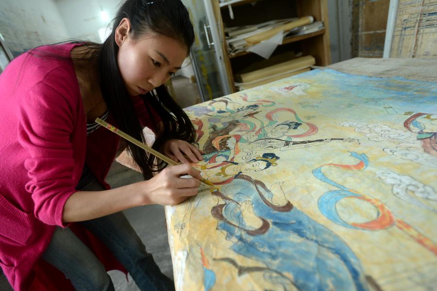Une jeune peintre dessine une peinture murale dans un studio de la commune de Yuequan, à Dunhuang, dans la Province du Gansu (Nord-ouest de la Chine), le 27 juin 2014. Attirés par l'art des peintures murales des Grottes de Mogao, de plus en plus de jeunes artistes viennent à Dunhuang pour apprendre la création de peintures murales et ouvrir leurs propres studios. [Photo / Xinhua] 