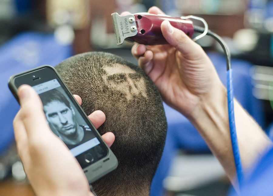 A partir d'une photo affichée sur son mobile, le coiffeur a commencé à « dessiner » l'image de Messi sur la tête de son client, lundi 30 juin 2014.