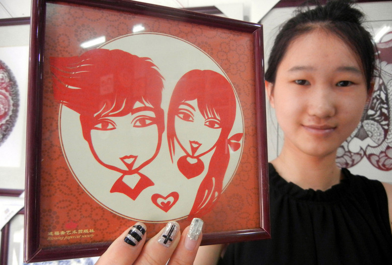 Une jeune fille montre une œuvre en papier découpé où figure le couple, dans la ville de Suzhou, dans la Province du Jiangsu, en Chine de l'Est, le 30 juillet 2014. 