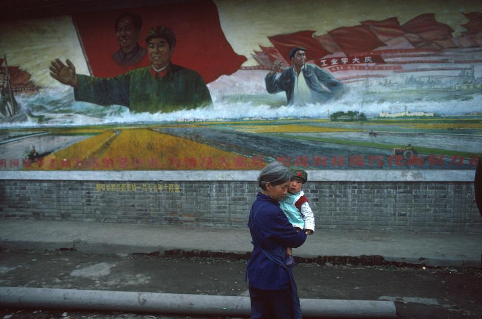 Portant un enfant dans ses bras, une vielle femme passe devant une affiche de Hua Guofeng à l’époque de la révolution culturelle, à Chengdu (1980).