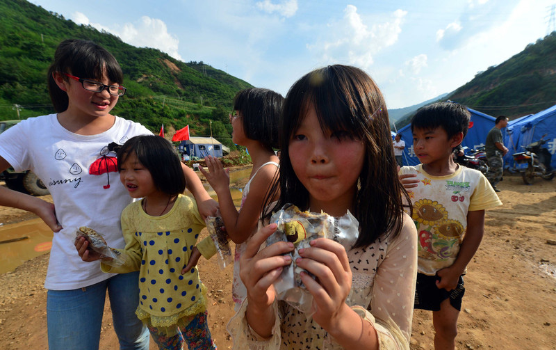 Des enfants dégustent des noix offertes par le commerçant Ouigour Adil Memettur sur un site de relogement du village de Longtoushan à Ludian, dans la province chinoise du Yunnan, le jeudi 7août 2014.