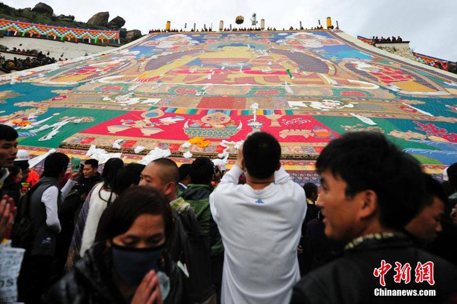 Les bouddhistes tibétains et les touristes admirent un tangka géant, une broderie ou peinture de soie religieuse propre au Tibet, lors du festival annuel de Shoton au monastère de Drepung à la périphérie de Lhassa, dans la région autonome du Tibet, le 25 août 2014 [Photo/Chinanews.com]