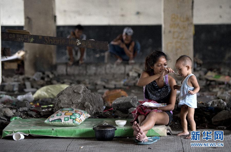 Le 28 août 2014, à Manille, une jeune femme donne à manger à un enfant sous un pont routier, l’endroit où elle vit. 