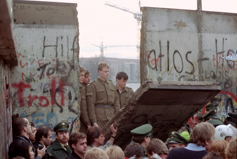 Des gardes-frontières est-allemands regardent à travers un trou sur le mur de Berlin après que des manifestants en aient abattu une partie de la paroi à la porte de Brandebourg, le 11 novembre 1989.