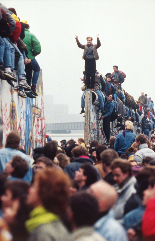 Des berlinois font la fête au sommet du mur tandis que les Allemands de l'Est, à l’arrière, passent par le mur de Berlin démantelé sur la Potsdamer Platz le 12 novembre, 1989.