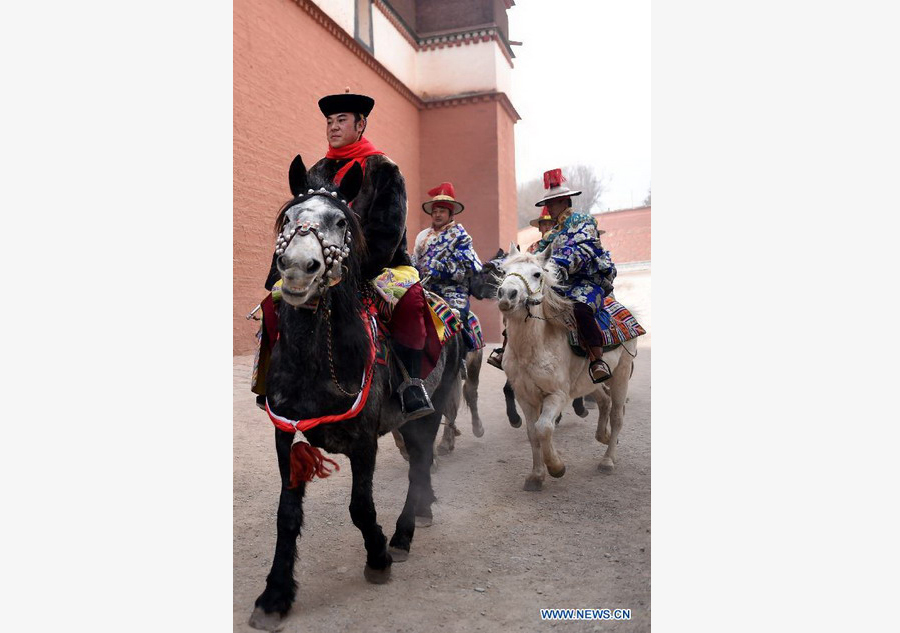 Des cavaliers attendent des lamas pour porter une énorme thangka (peinture religieuse tibétaine) vers une colline pour le rituel annuel au monastère de Labrang à Xiahe, dans la province chinoise du Gansu (nord-ouest du pays), le 3 mars 2015. [Photo/Xinhua]