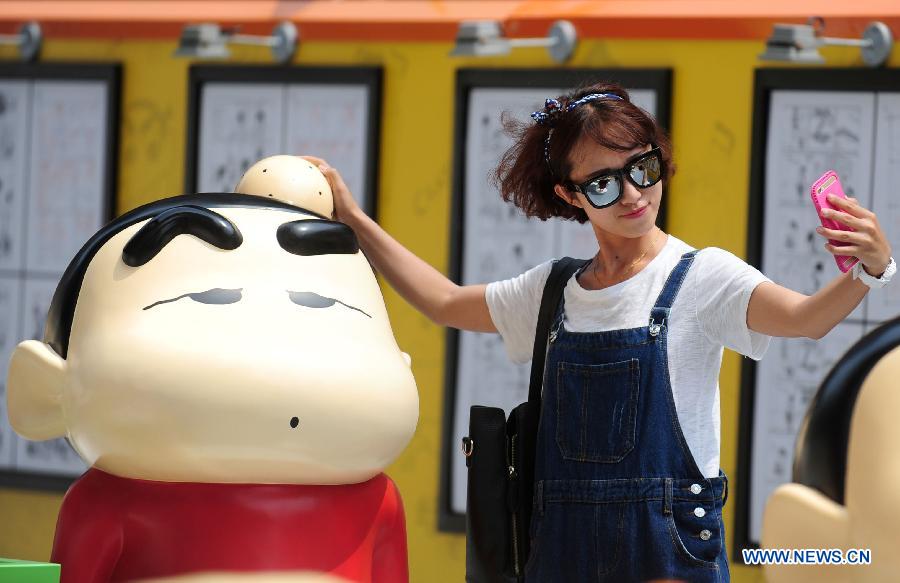 Une fille prend un selfie avec une statue de Crayon Shin-chan, une série japonaise de manga et d'anime créée par Yoshito Usui en 1990, lors d'une exposition pour célébrer le 25ème anniversaire du personnage, à Shenyang, capitale de la province du Liaoning, le 11 juillet 2015. (Xinhua)
