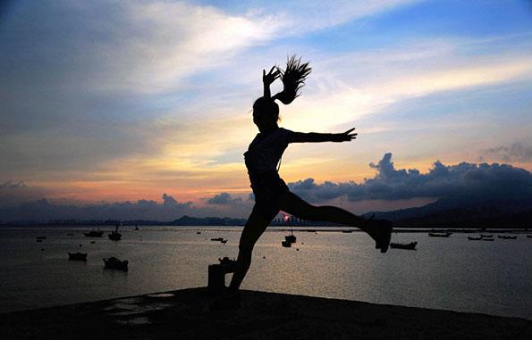 Une touriste saute devant le soleil qui se lève en arrière-plan à Qingdao, dans la Province du Shandong, le 10 août 2015. [Photo / IC]