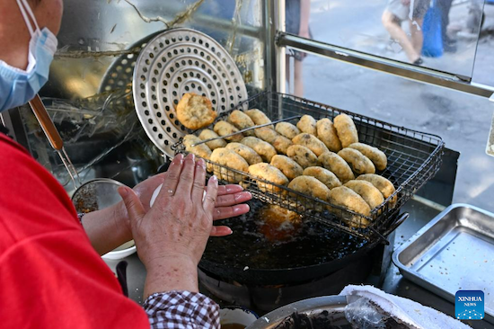 Une dame prépare des zhagao à son stand. Ces beignets de riz glutineux renferment une farce de pâte de haricot rouge sucrée. (Xinhua/Sun Fanyue)