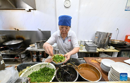 Une employée prépare un guobacai. Ce plat est composé de fines crêpes de farines de haricot et de millet, coupées en forme de nouilles et plongées dans une sauce à base d’huile de sésame, de gingembre, d’oignons verts, de sauce soja, de tofu fermenté, d’huile pimentée, de coriandre,… (Xinhua/Sun Fanyue)