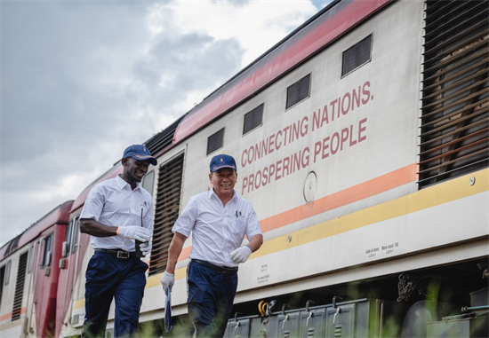 L'instructeur chinois Jiang Liping (à droite) et son apprenti Horace Owiti passent devant un wagon du chemin de fer Mombasa-Nairobi avec un slogan imprimé "connecter les nations, faire prospérer le peuple" à Nairobi, au Kenya, le 23 mai 2023. (Xinhua/Wang Guansen)