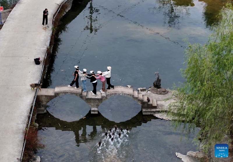 Photo aérienne prise par un drone le 1er novembre 2025 montrant des touristes posant pour des photos sur un petit pont dans un village du canton de Jinde, à Liuzhou, dans la région autonome Zhuang du Guangxi (sud de la Chine). (Xinhua/Huang Xiaobang)