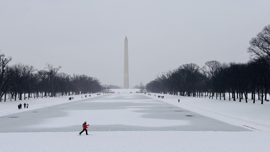 Une personne marche dans la neige près du Miroir d'eau devant le Mémorial de Lincoln à Washington DC, aux Etats-Unis, le 25 janvier 2026. (Xinhua/Xu Jianmei)
