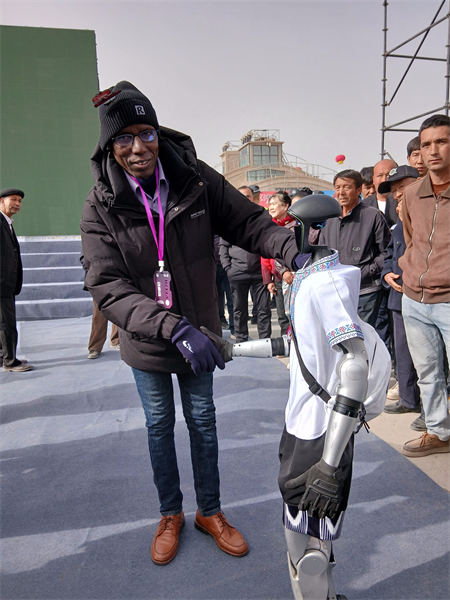 Aliu Baldé interagit avec un robot humanoïde lors de la cérémonie d'ouverture de la 11e Foire des fruits spécialisés du Xinjiang (Aksu), dans la région autonome ouïgoure du Xinjiang (nord-ouest de la Chine). (Photo fournie par la personne interviewée)